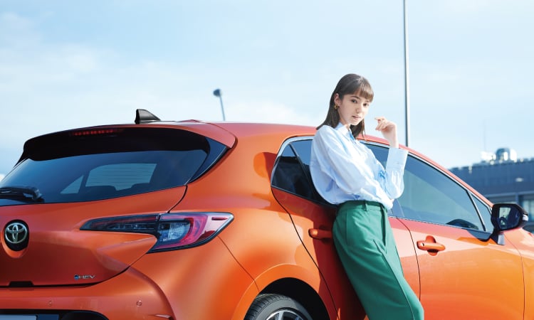 カローラ スポーツ G“Z”。ボディカラーはオレンジマイカメタリック。車の横に立つ女性の様子。