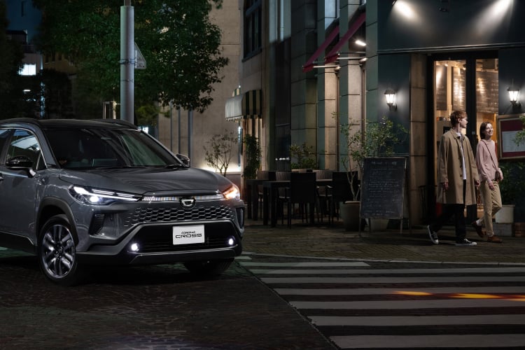 夜の街角の横断歩道前で一時停止するカローラクロス Z(2WD)と歩道を歩く男女